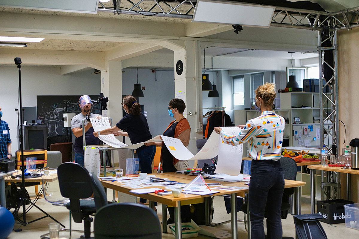 4 Menschen stehen im Medienlanbor und haben eine Papierbahn in den Händen