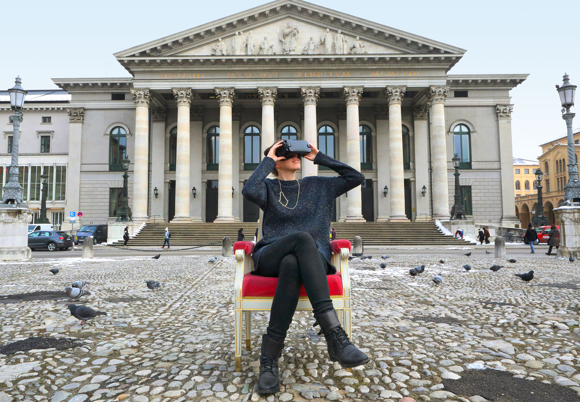 Frau sitzt mit Virtual-Reality-Brille vor der Bayerischen Staatsoper
